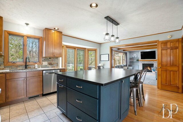 kitchen with stainless steel dishwasher, a kitchen breakfast bar, a sink, a warm lit fireplace, and a kitchen island