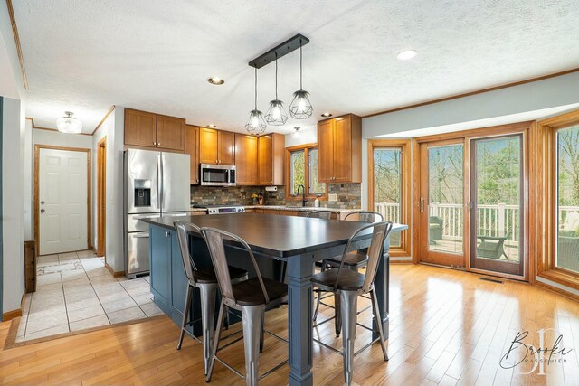 kitchen with stainless steel appliances, visible vents, brown cabinetry, a sink, and light wood-style flooring