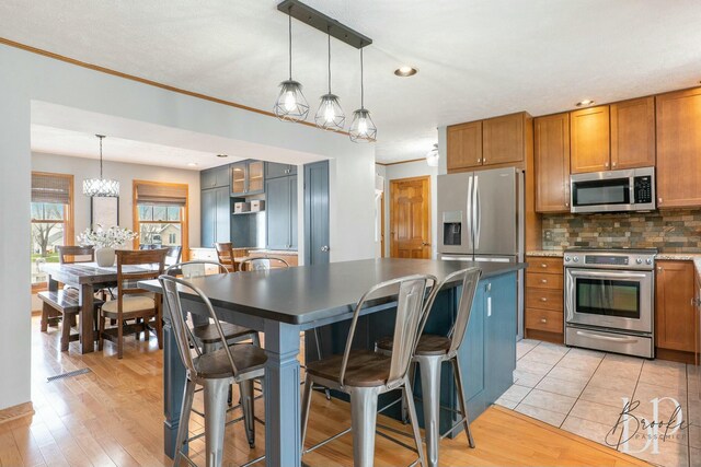 kitchen with stainless steel appliances, tasteful backsplash, light wood-type flooring, a notable chandelier, and brown cabinets