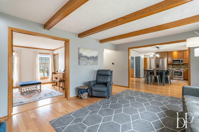 living area with light wood-type flooring, baseboards, and beamed ceiling