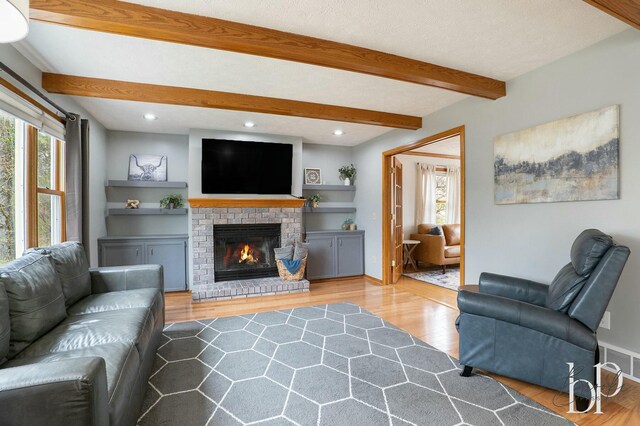 living area featuring beamed ceiling, wood finished floors, visible vents, and a fireplace