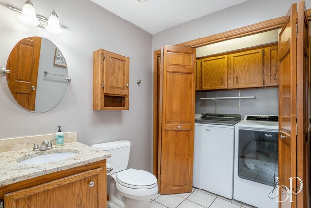 half bathroom with vanity, separate washer and dryer, toilet, and tile patterned flooring