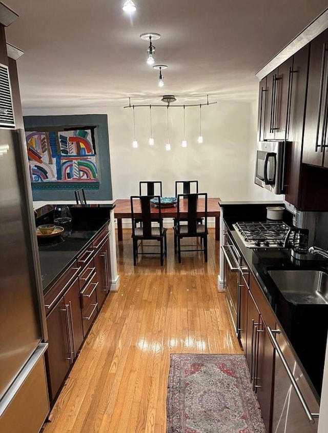 kitchen featuring dark countertops, dark brown cabinets, a sink, light wood-type flooring, and appliances with stainless steel finishes