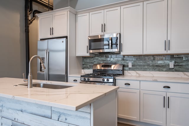 kitchen with light stone counters, tasteful backsplash, a sink, white cabinets, and appliances with stainless steel finishes