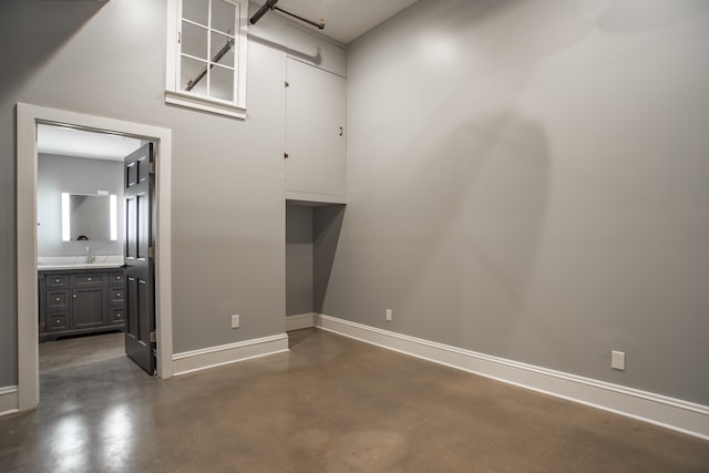 unfurnished room featuring baseboards, a sink, and finished concrete flooring