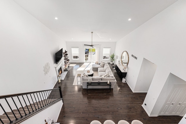 living room featuring baseboards, a lit fireplace, dark wood-type flooring, recessed lighting, and a ceiling fan