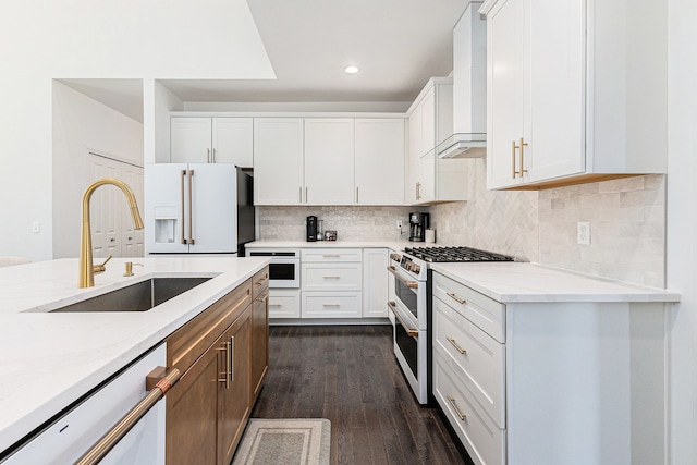 kitchen with white appliances, light stone countertops, wall chimney exhaust hood, a sink, and dark wood finished floors