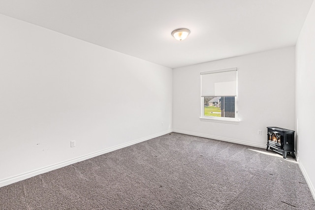 carpeted empty room featuring baseboards and a wood stove