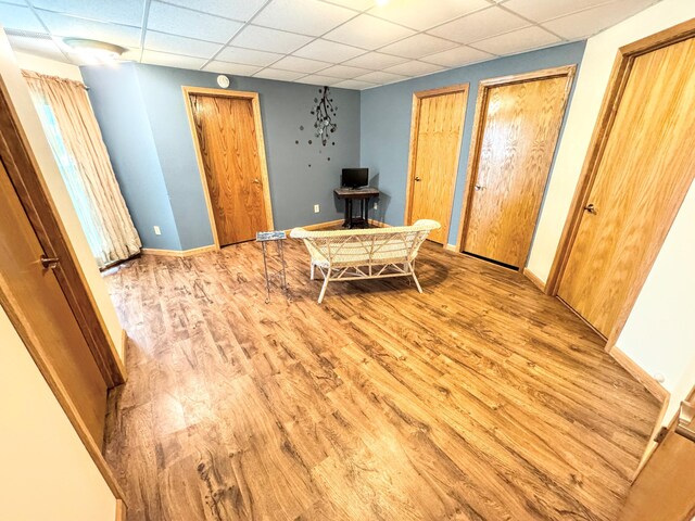 living area with wood finished floors, a drop ceiling, and baseboards