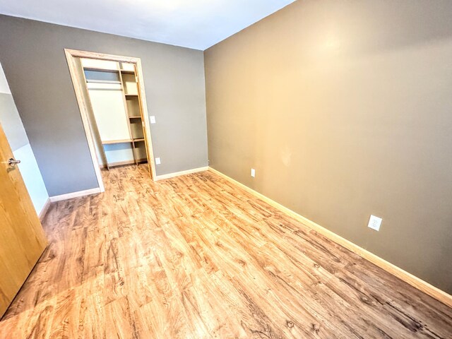 unfurnished bedroom with baseboards, wood finished floors, a closet, and a walk in closet