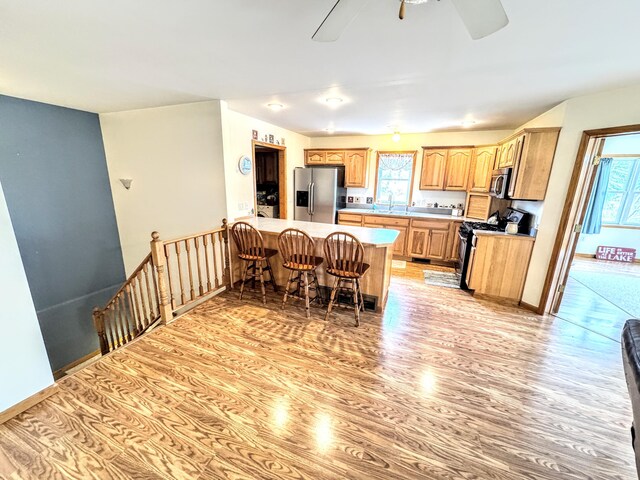 kitchen with stainless steel appliances, light countertops, light wood-style floors, a peninsula, and a kitchen bar