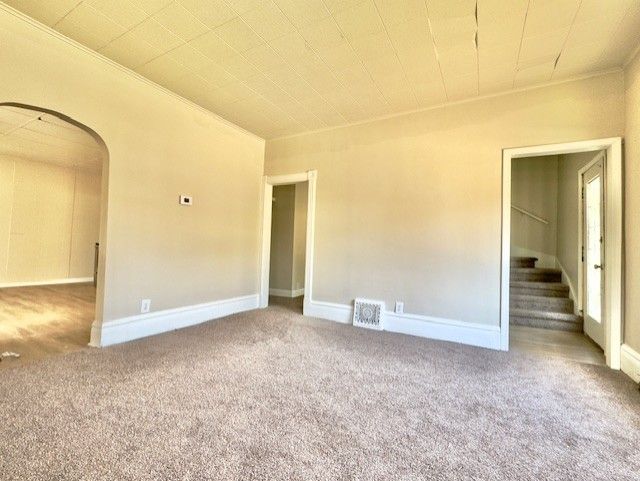 empty room with stairway, crown molding, arched walkways, carpet floors, and visible vents