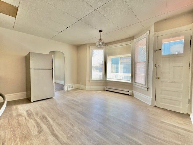 unfurnished dining area with a baseboard radiator, arched walkways, light wood finished floors, baseboards, and a paneled ceiling