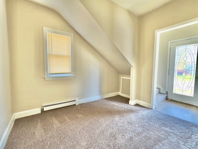 additional living space featuring a baseboard heating unit, lofted ceiling, carpet flooring, and baseboards