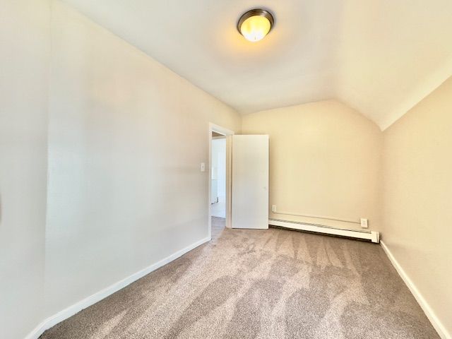 unfurnished room featuring lofted ceiling, baseboards, carpet floors, and a baseboard radiator
