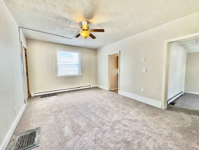 carpeted spare room with baseboard heating, ceiling fan, a textured ceiling, and visible vents