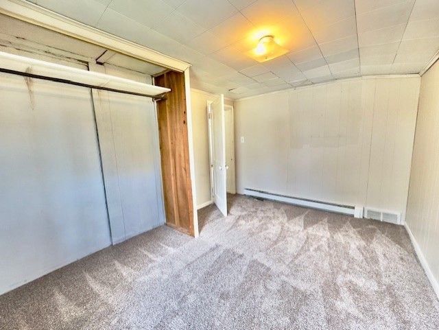 unfurnished bedroom with a baseboard radiator, a closet, carpet, and visible vents
