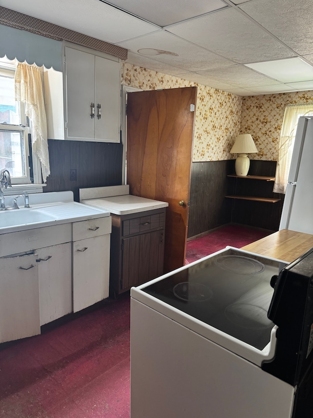 kitchen with white appliances, light countertops, wallpapered walls, a paneled ceiling, and a sink