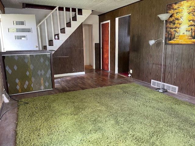 unfurnished living room featuring wood finished floors, stairway, wooden walls, and baseboards