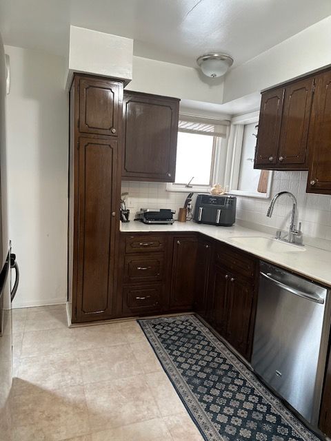 23226 Edward St, Dearborn, MI 48128 - kitchen with stainless steel dishwasher, a sink, light countertops, tasteful backsplash, and dark brown cabinetry
