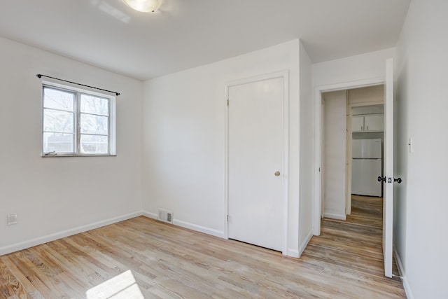 unfurnished bedroom with visible vents, freestanding refrigerator, a closet, light wood-style floors, and baseboards