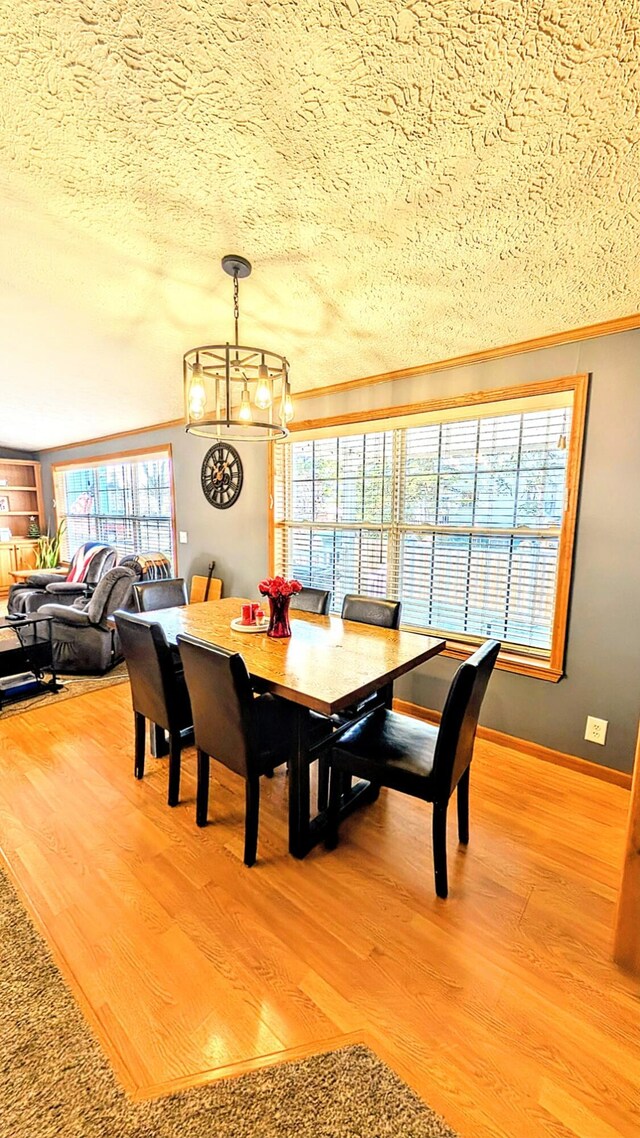 dining room featuring light wood-type flooring, a textured ceiling, ornamental molding, and an inviting chandelier