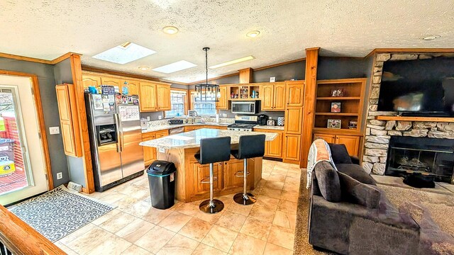 kitchen featuring lofted ceiling with skylight, open floor plan, stainless steel appliances, light countertops, and ornamental molding
