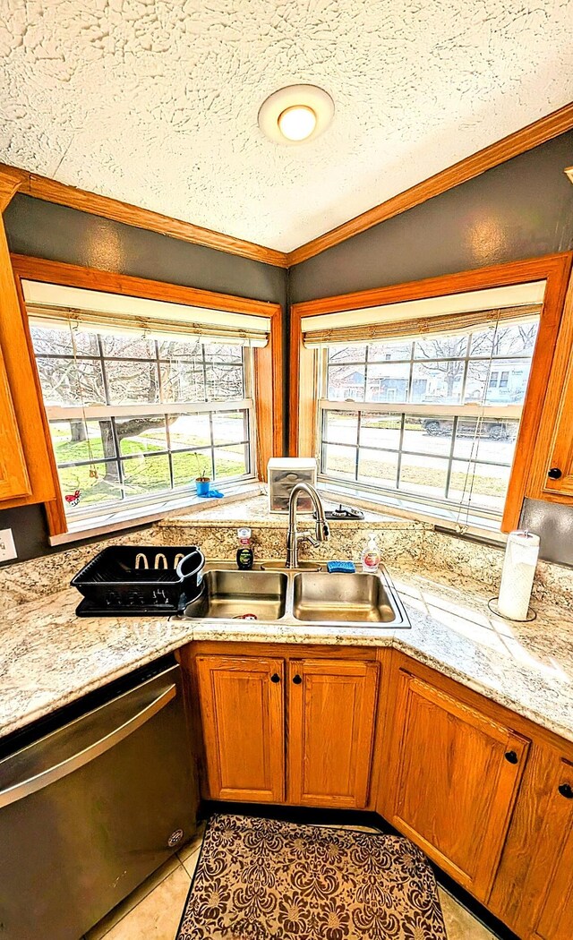 kitchen featuring stainless steel dishwasher, ornamental molding, light tile patterned floors, a sink, and brown cabinetry