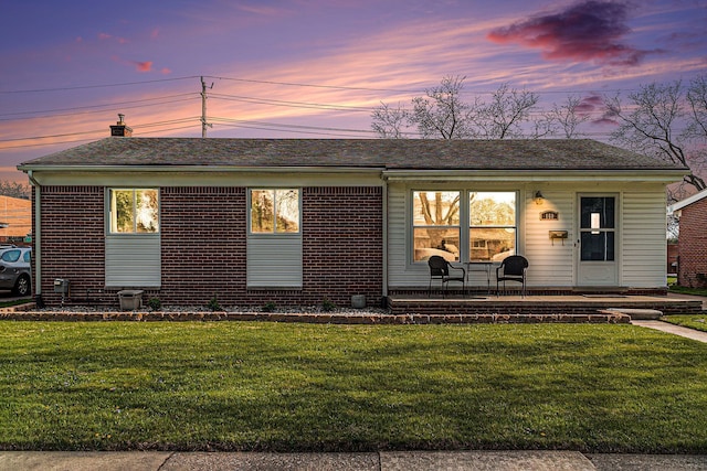 ranch-style house with a yard, brick siding, a chimney, and a shingled roof