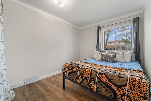 bedroom with crown molding, baseboards, wood finished floors, and visible vents