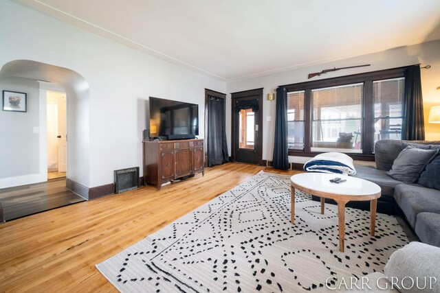 living area with arched walkways, wood finished floors, visible vents, and baseboards