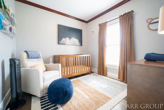 bedroom featuring baseboards, a nursery area, wood finished floors, and ornamental molding