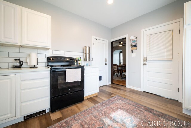 kitchen with black electric range oven, wood finished floors, white cabinets, and tasteful backsplash