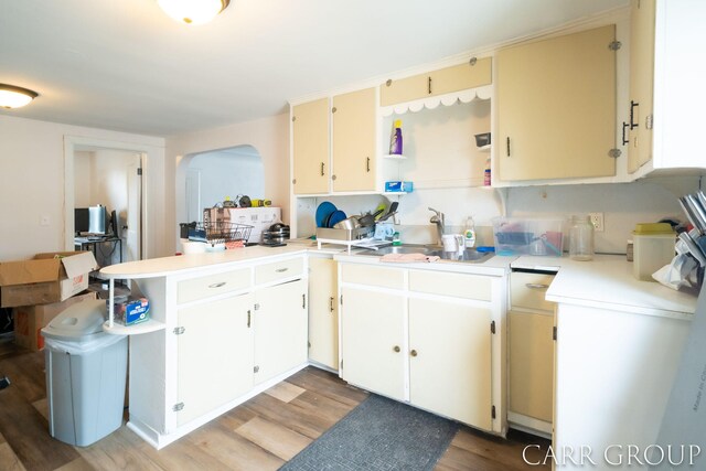 kitchen featuring a sink, light wood-style floors, arched walkways, light countertops, and a peninsula