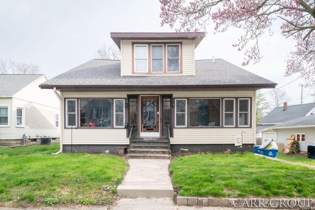 bungalow-style home with cooling unit, a shingled roof, and a front lawn