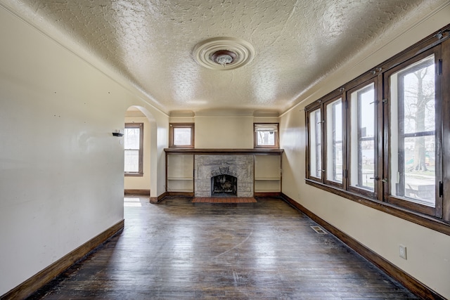 unfurnished living room featuring arched walkways, a textured ceiling, a stone fireplace, and hardwood / wood-style floors