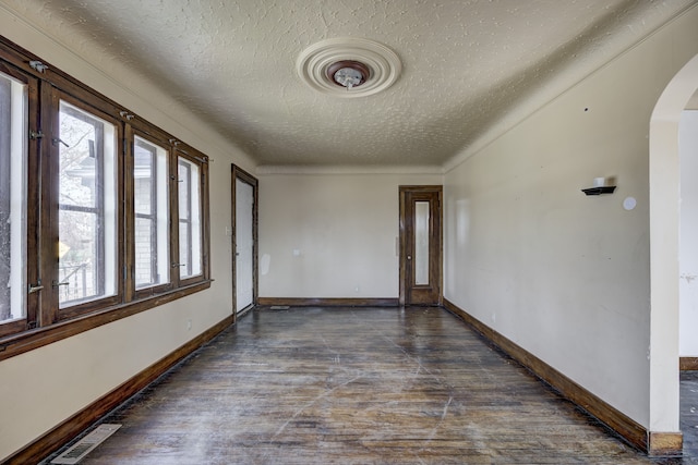 empty room featuring visible vents, arched walkways, a textured ceiling, and baseboards