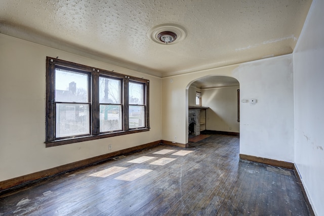 spare room featuring a fireplace, baseboards, a textured ceiling, hardwood / wood-style flooring, and arched walkways