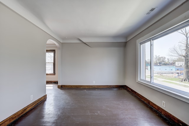 spare room featuring visible vents, arched walkways, baseboards, and hardwood / wood-style flooring