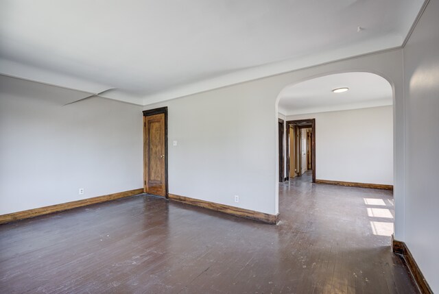 unfurnished room with baseboards, arched walkways, and wood finished floors