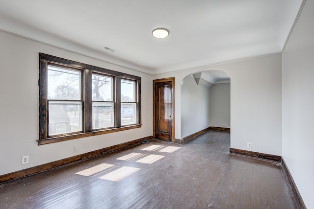 unfurnished room featuring wood-type flooring, arched walkways, baseboards, and visible vents