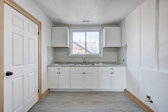 kitchen with visible vents, baseboards, light wood-style floors, white cabinets, and a sink