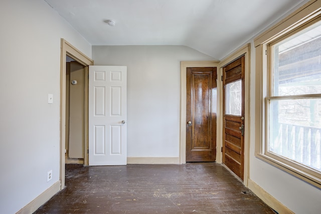 unfurnished bedroom featuring baseboards, lofted ceiling, multiple windows, and wood finished floors