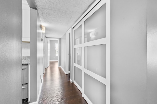 hallway with baseboards, a textured ceiling, and dark wood-type flooring