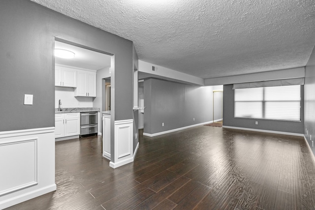 unfurnished living room featuring a textured ceiling, visible vents, dark wood finished floors, a sink, and a wainscoted wall