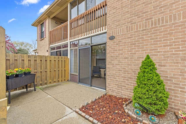 view of exterior entry with fence, a patio, and brick siding