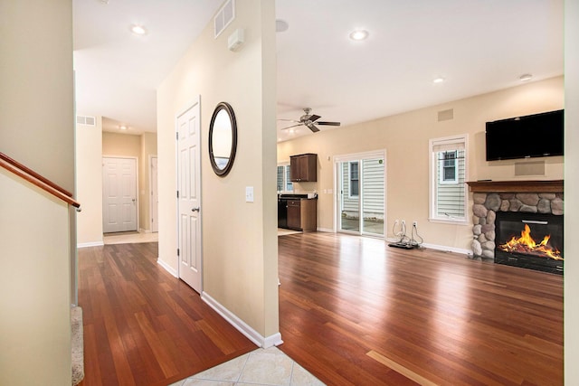 interior space with a stone fireplace, a ceiling fan, wood finished floors, and visible vents