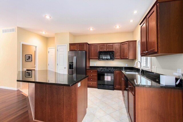 kitchen featuring visible vents, a sink, black microwave, stainless steel fridge, and range