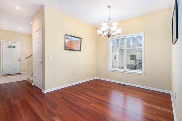 spare room with stairway, an inviting chandelier, wood finished floors, and visible vents