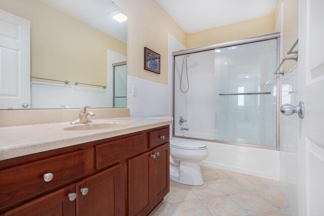 bathroom featuring tile patterned floors, vanity, tile walls, toilet, and shower / bath combination with glass door